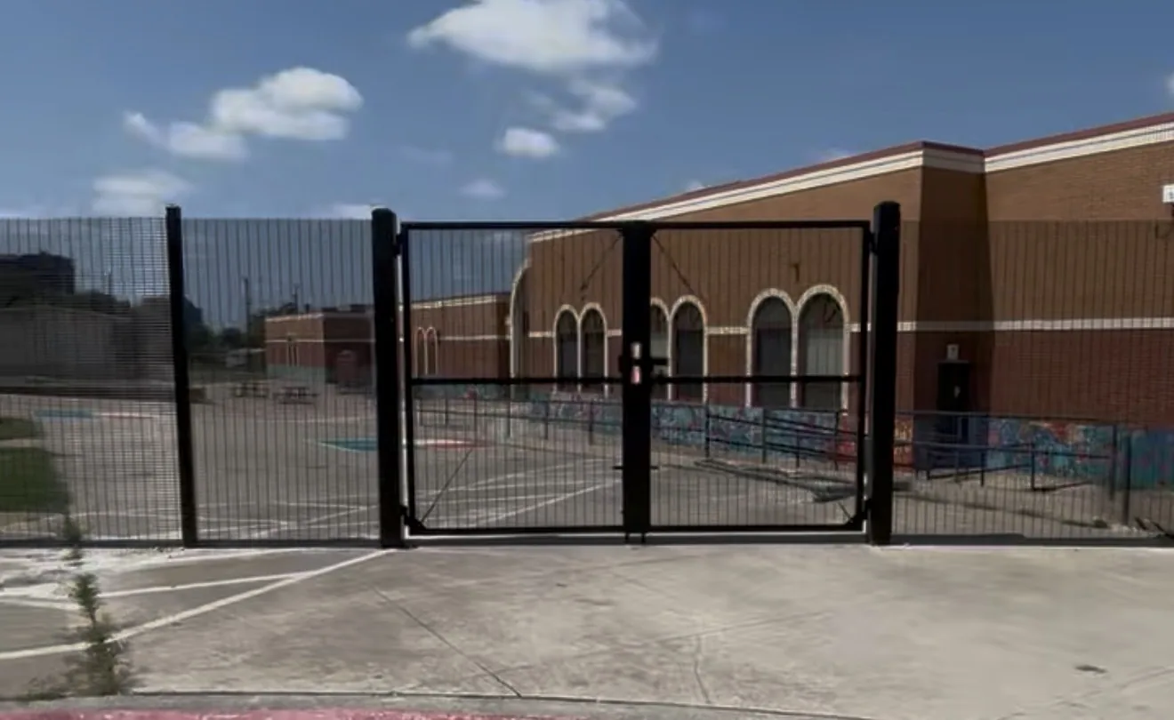 Black welded-mesh security fencing and double pedestrian gate at a brick campus building